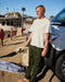 Man wearing white short-sleeved t-shirt and camo pants leaning on a car