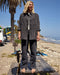 Person standing on a wooden bench at the beach with palm trees and ocean in the background