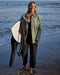 A woman wearing a green blanket shirt on the beach with ocean waves in the background